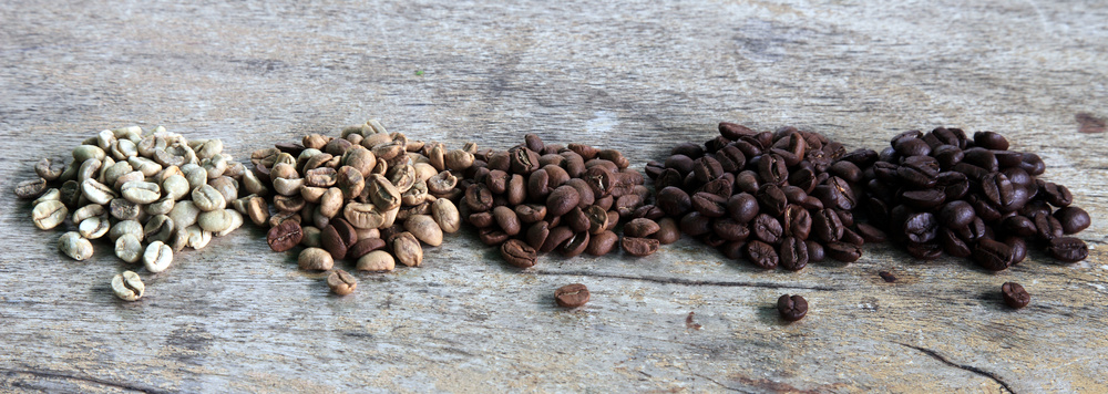 Kaffeebohnen in den unterschiedlichen Röststufen auf rustikaler Holzplatte.